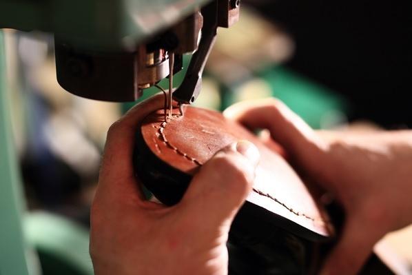 Detalhe de pessoa costurando sapato em máquina industrial